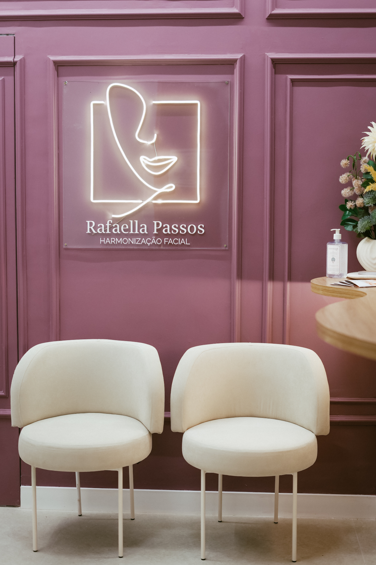 Recepção do consultório com poltronas claras e identidade da Dra. Rafaella em parede malva